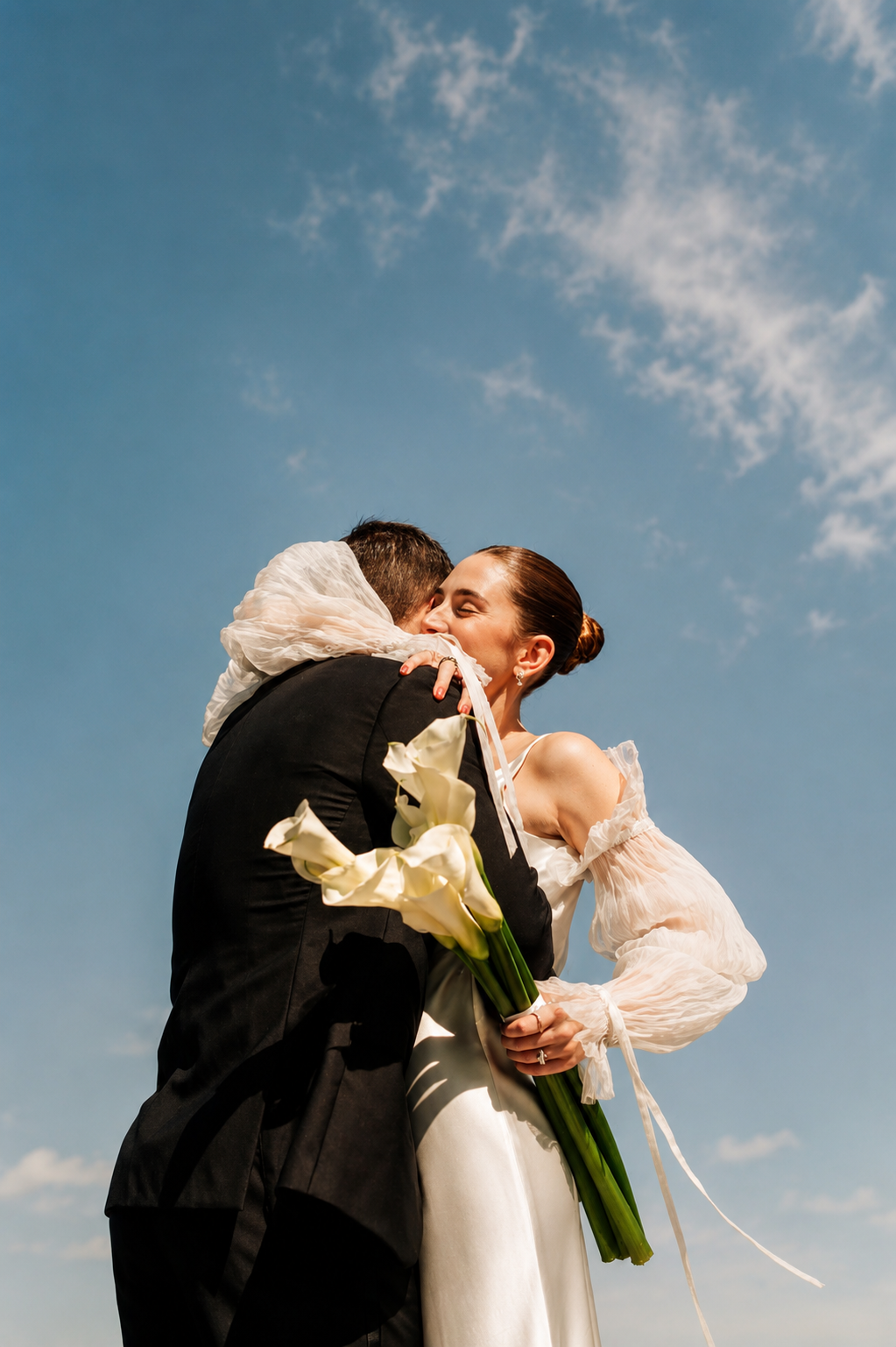 Novios abrazados bajo el cielo con ramo de calas — reportaje de boda natural en Valencia